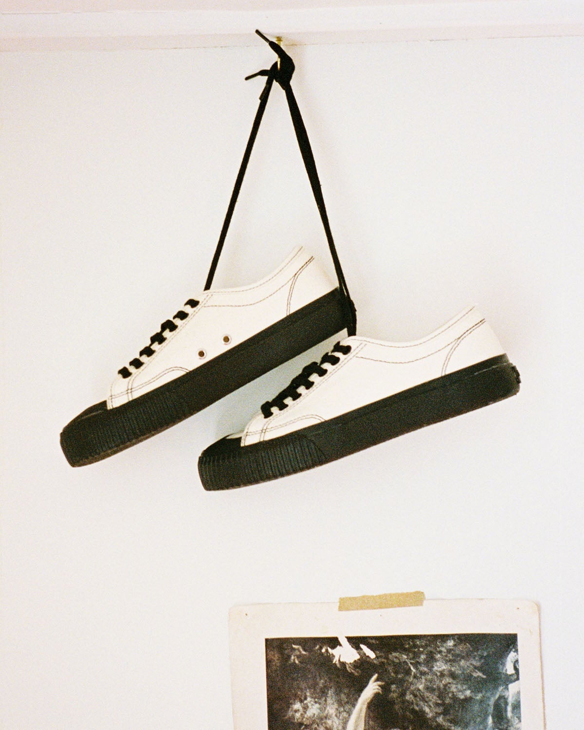 Buddy x CC Hemp Off-White/Black trainers hanging by their black laces from a hook on a white wall