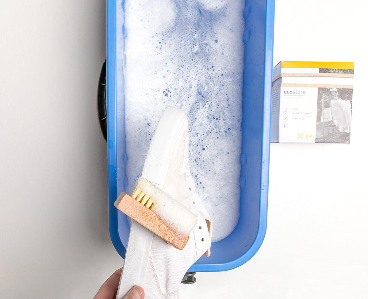 White Collective Canvas trainers being held above soapy water in a blue bucket.