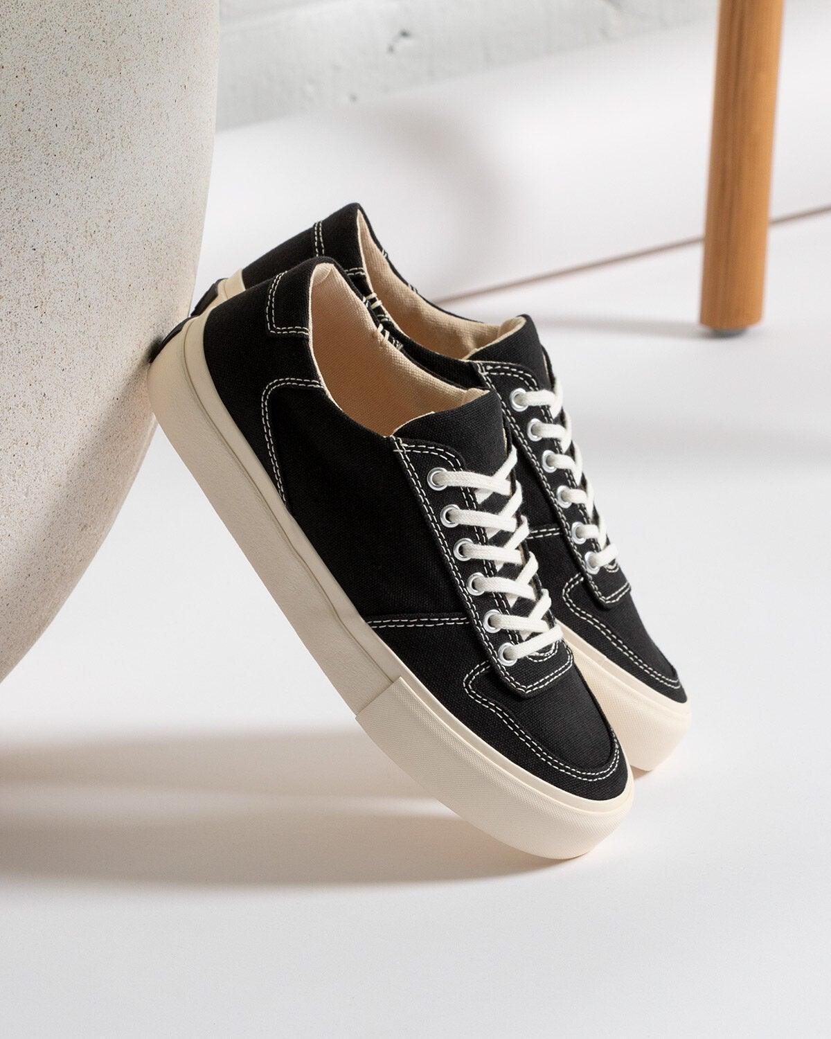 Pair of Bal Black/White trainers leaning against a white rounded form in a bright room