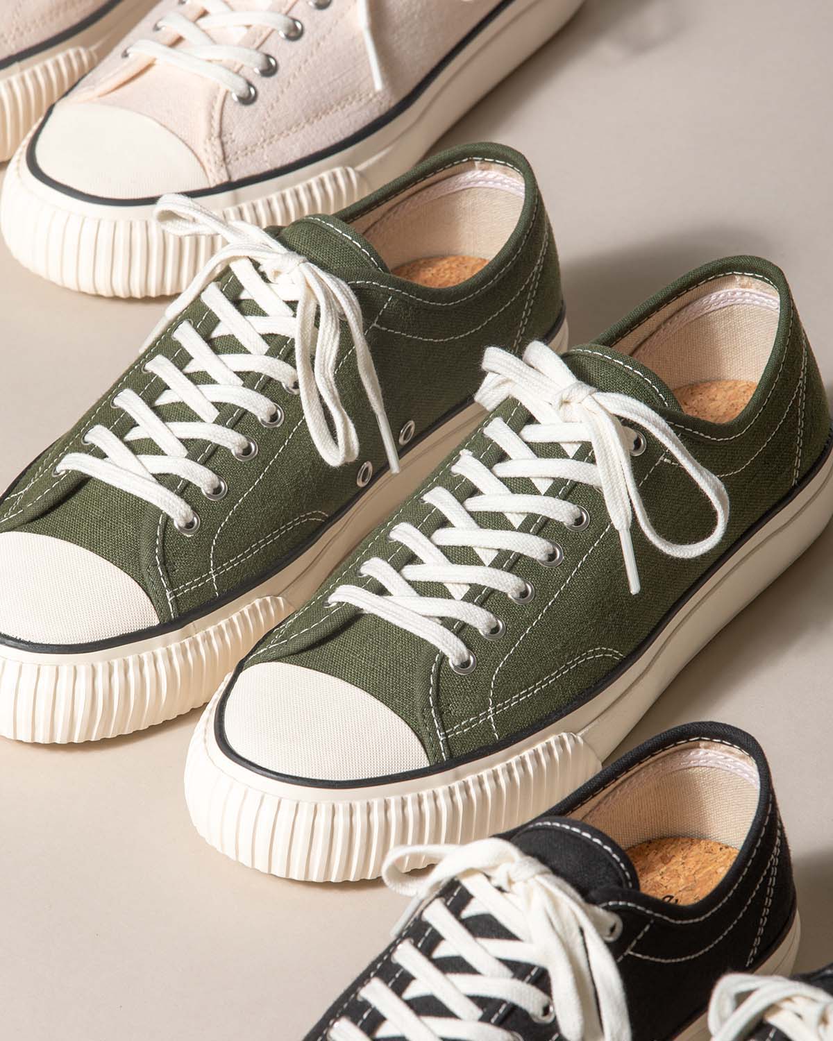 Straat Hemp Olive trainers beside Natural/Black and Black/White pairs on a beige backdrop