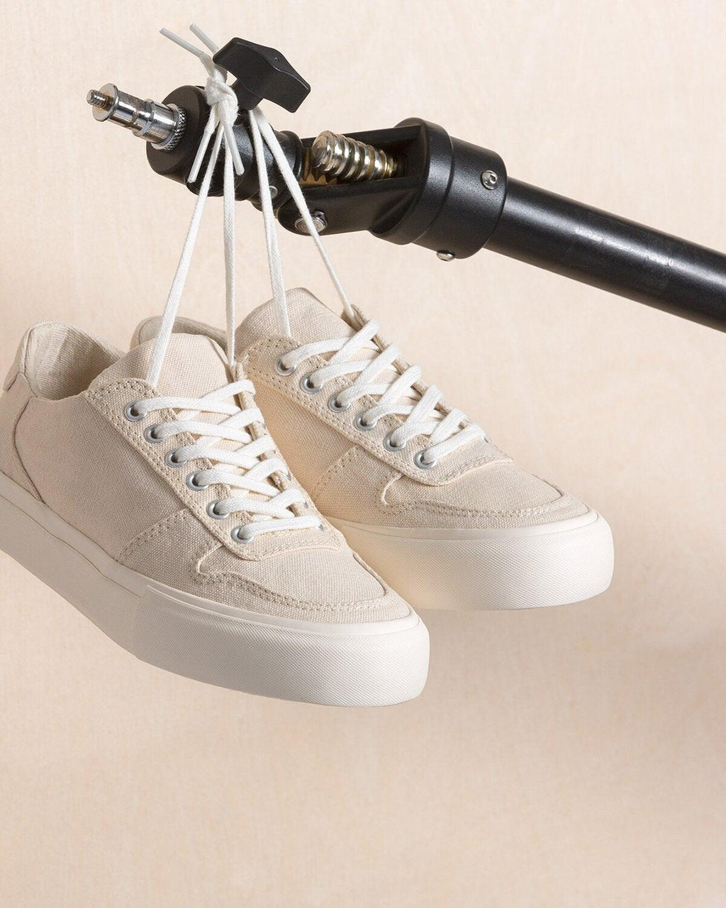 Pair of Bal Natural trainers hanging by their laces from a studio light stand clamp