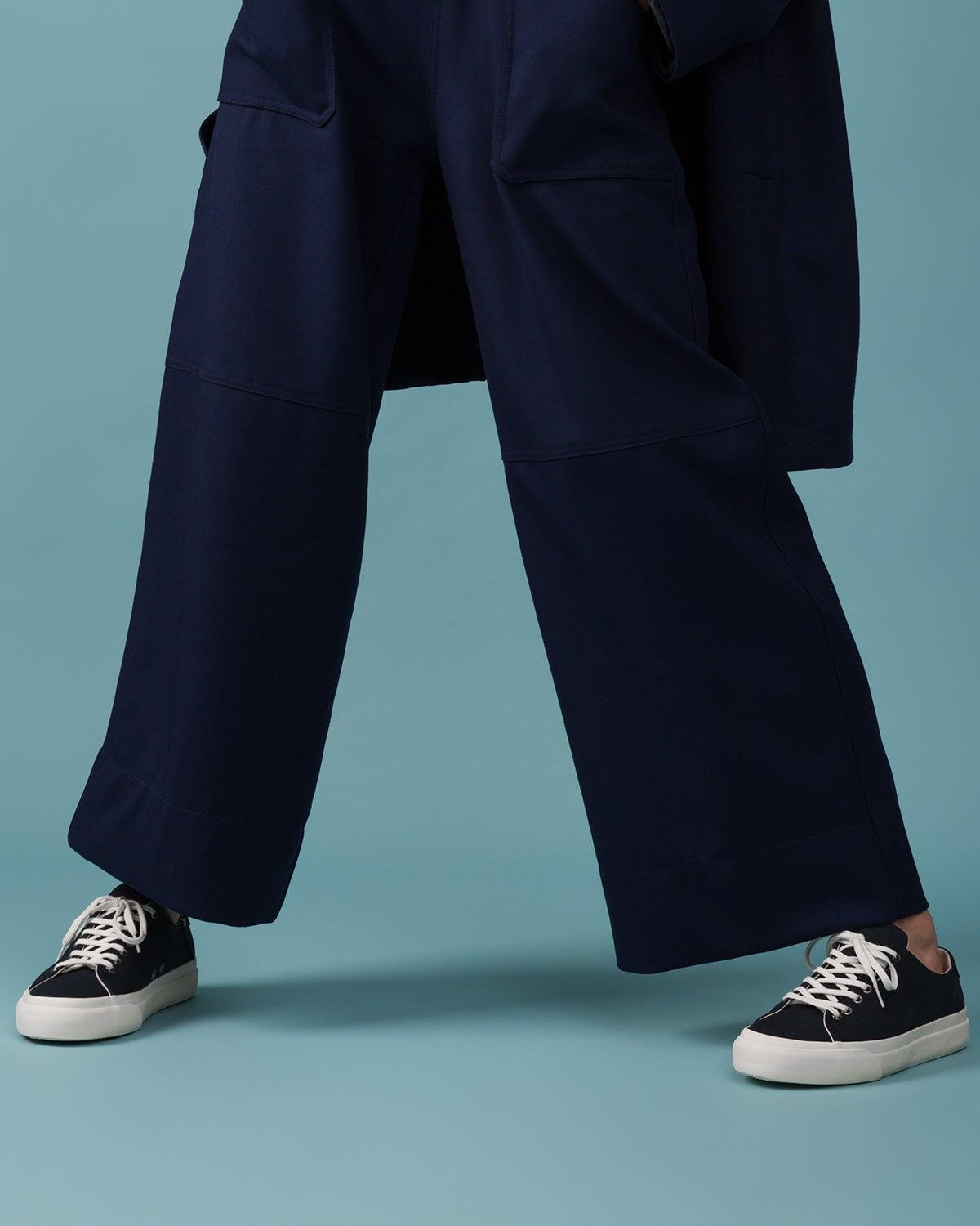 Wearing Baan Navy trainers with wide-leg navy trousers against a teal backdrop