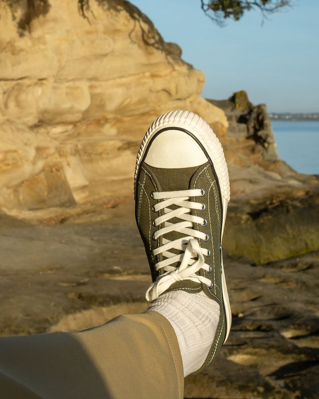 Wearing Straat Hemp Olive trainers with white socks and khaki trousers by sandstone rocks and water