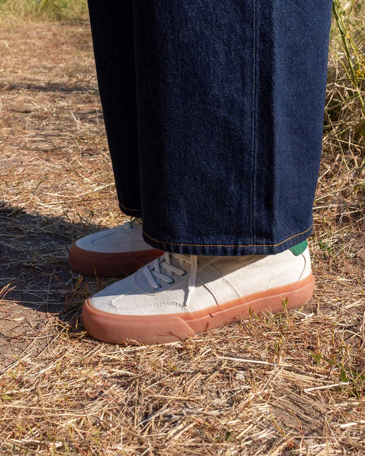 Wearing Veld Hemp Ecru/Sage trainers with wide-leg raw denim on a dry grass path
