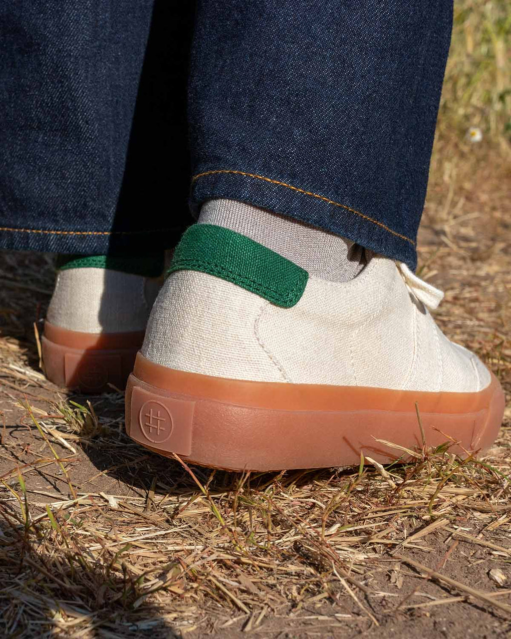 Veld Hemp Ecru/Sage trainers worn with grey socks and dark denim, rear view showing green heel tabs
