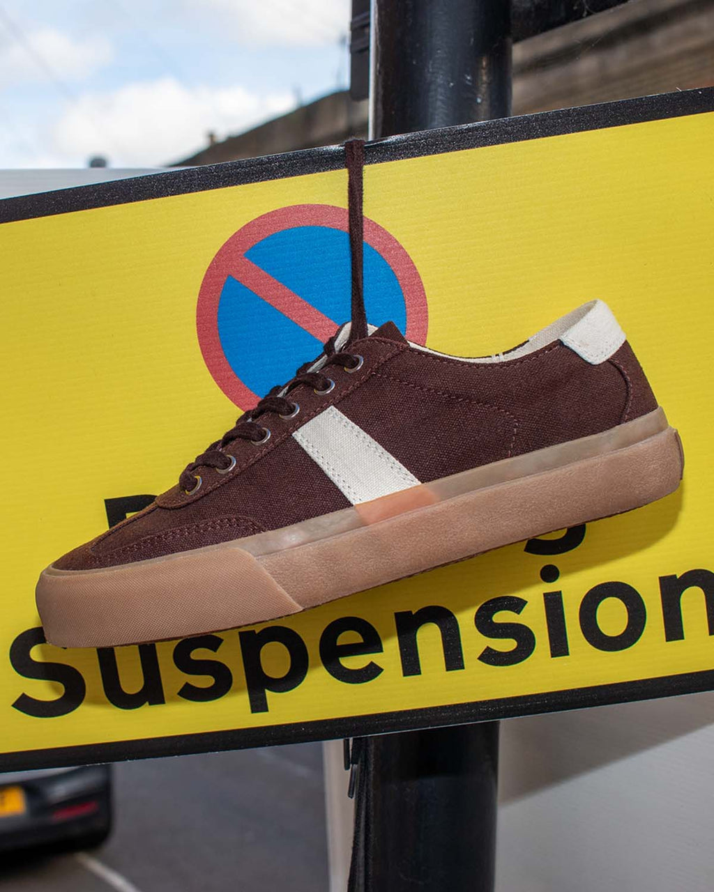 Veld Hemp Coffee/Ecru trainer hanging by its laces from a yellow parking suspension sign