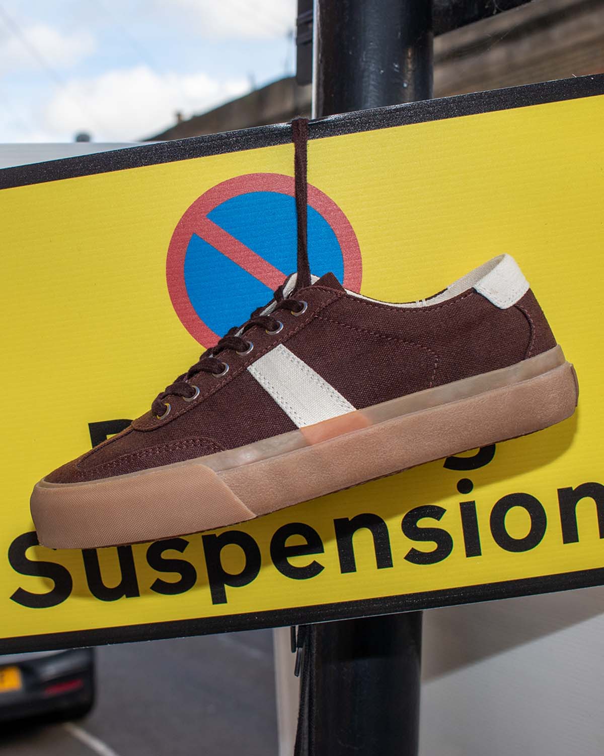 Veld Hemp Coffee/Ecru trainer hanging by its laces from a yellow parking suspension sign