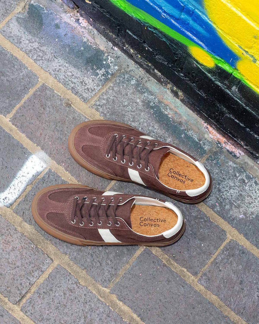 Pair of Veld Hemp Coffee/Ecru trainers from above on grey brick paving beside a graffiti wall