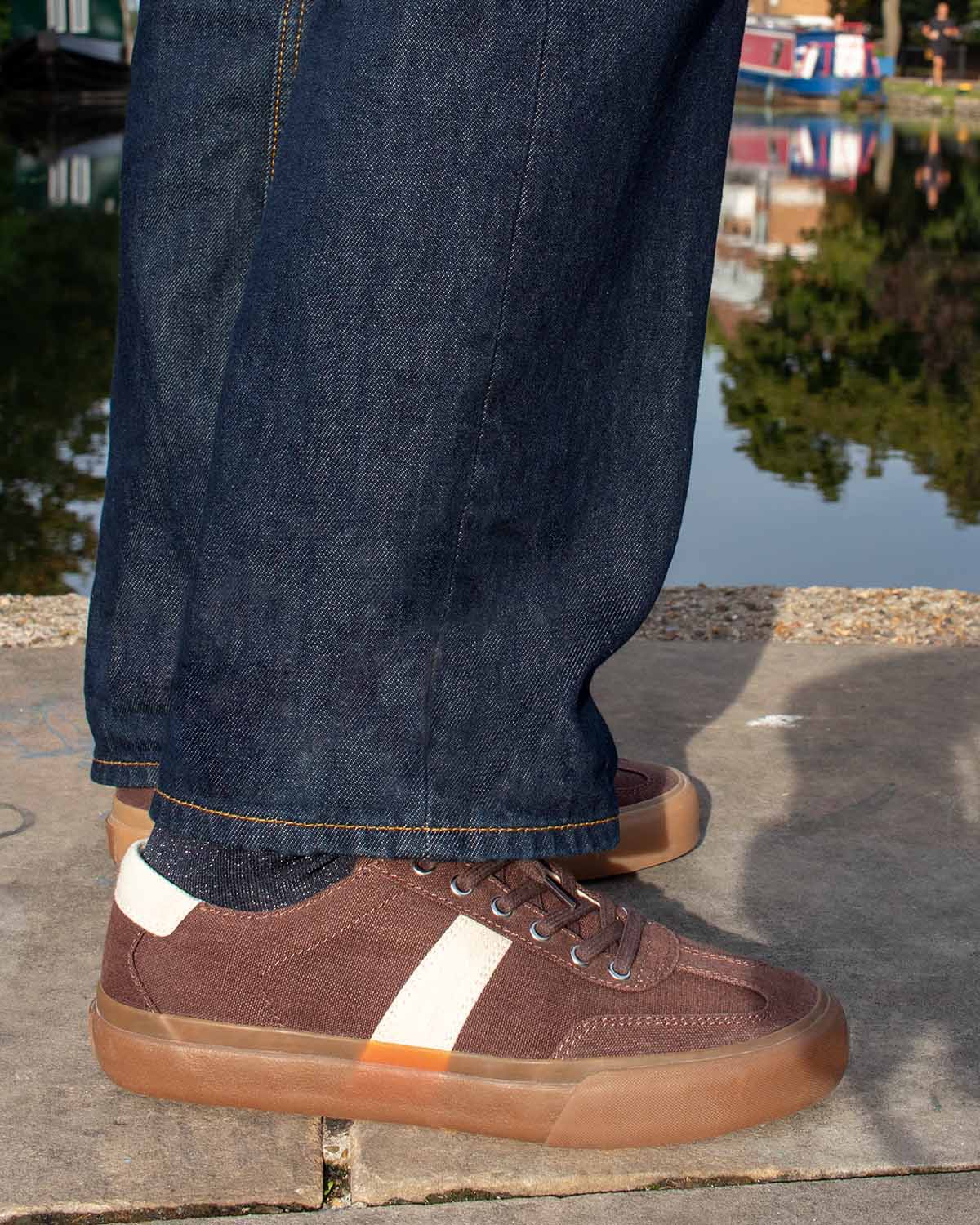 Veld Hemp Coffee/Ecru trainers worn with dark raw denim beside a canal