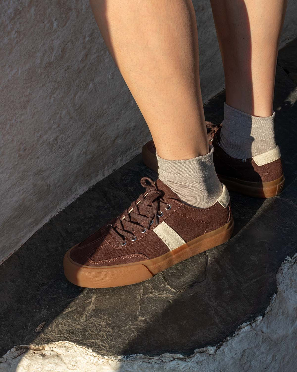 Veld Hemp Coffee/Ecru trainers worn with grey socks, standing on a stone ledge