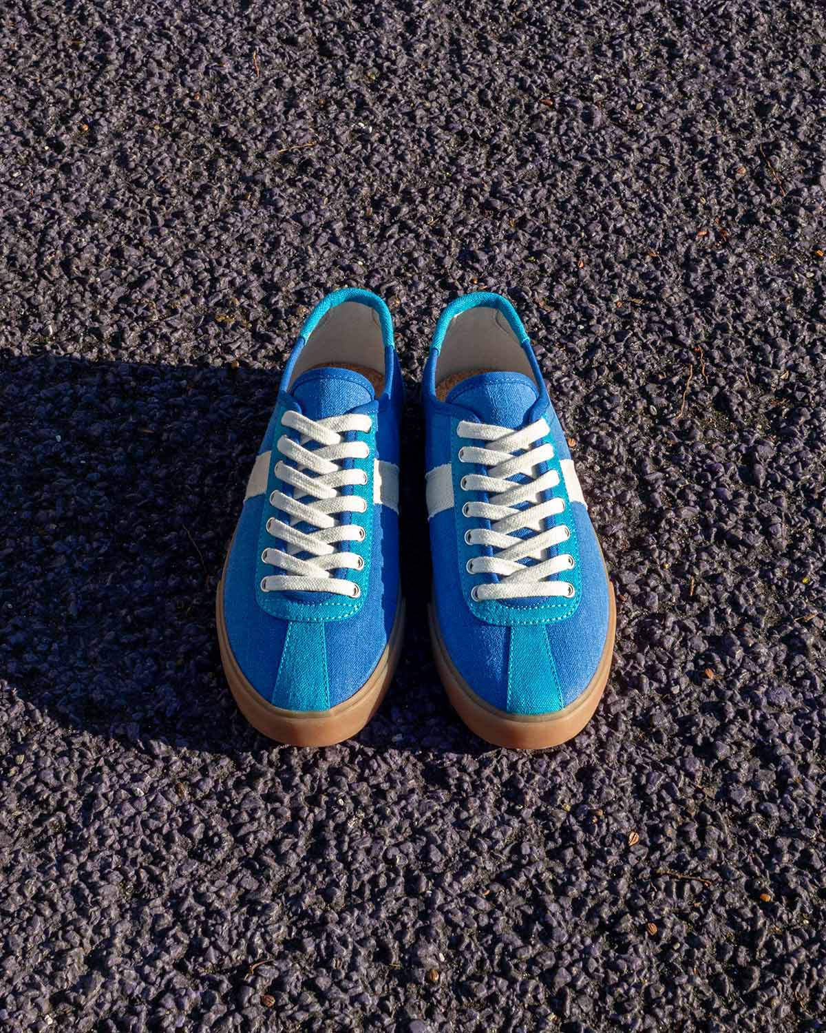 Looper Hemp Blue trainers, front view of the pair standing on dark asphalt in sunlight