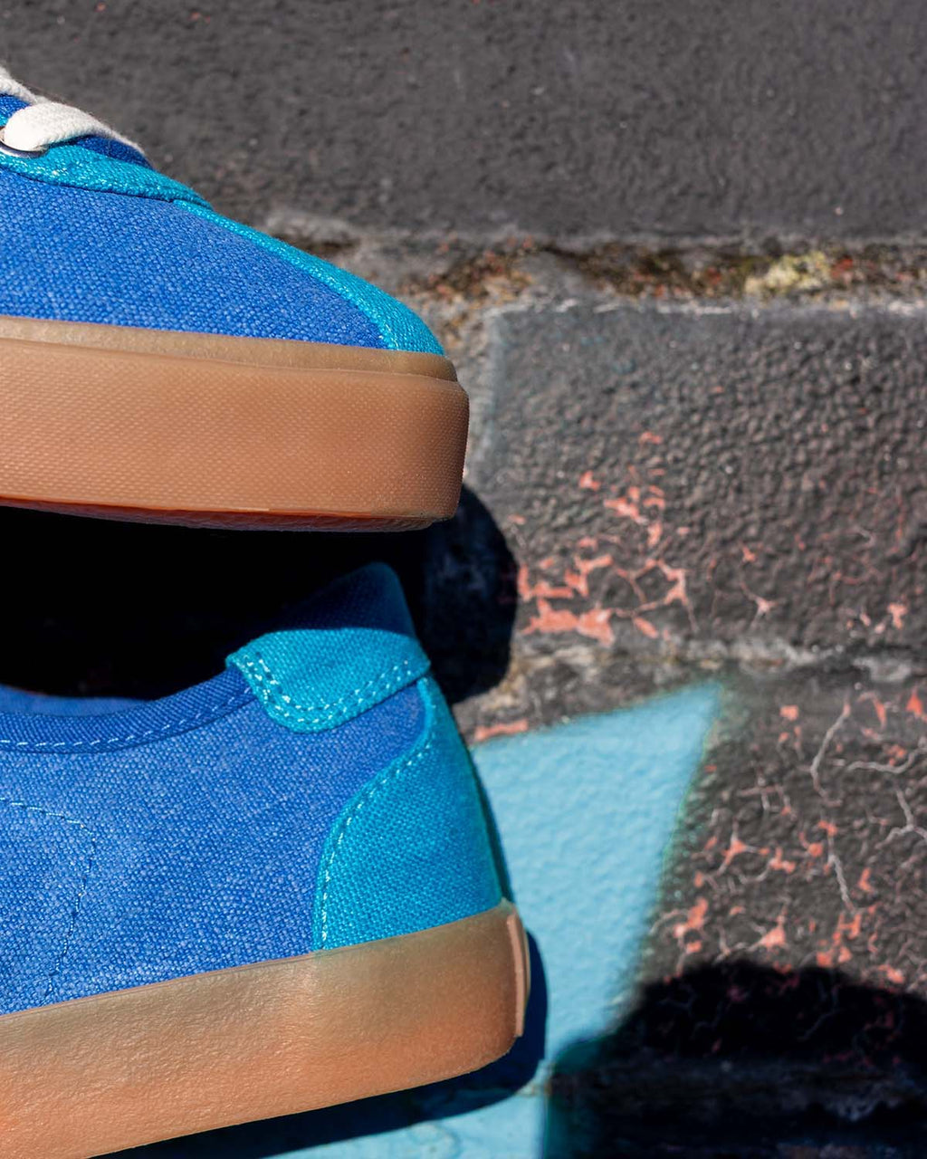 Close-up of two Looper Hemp Blue trainers stacked against a brick wall, showing natural gum rubber soles