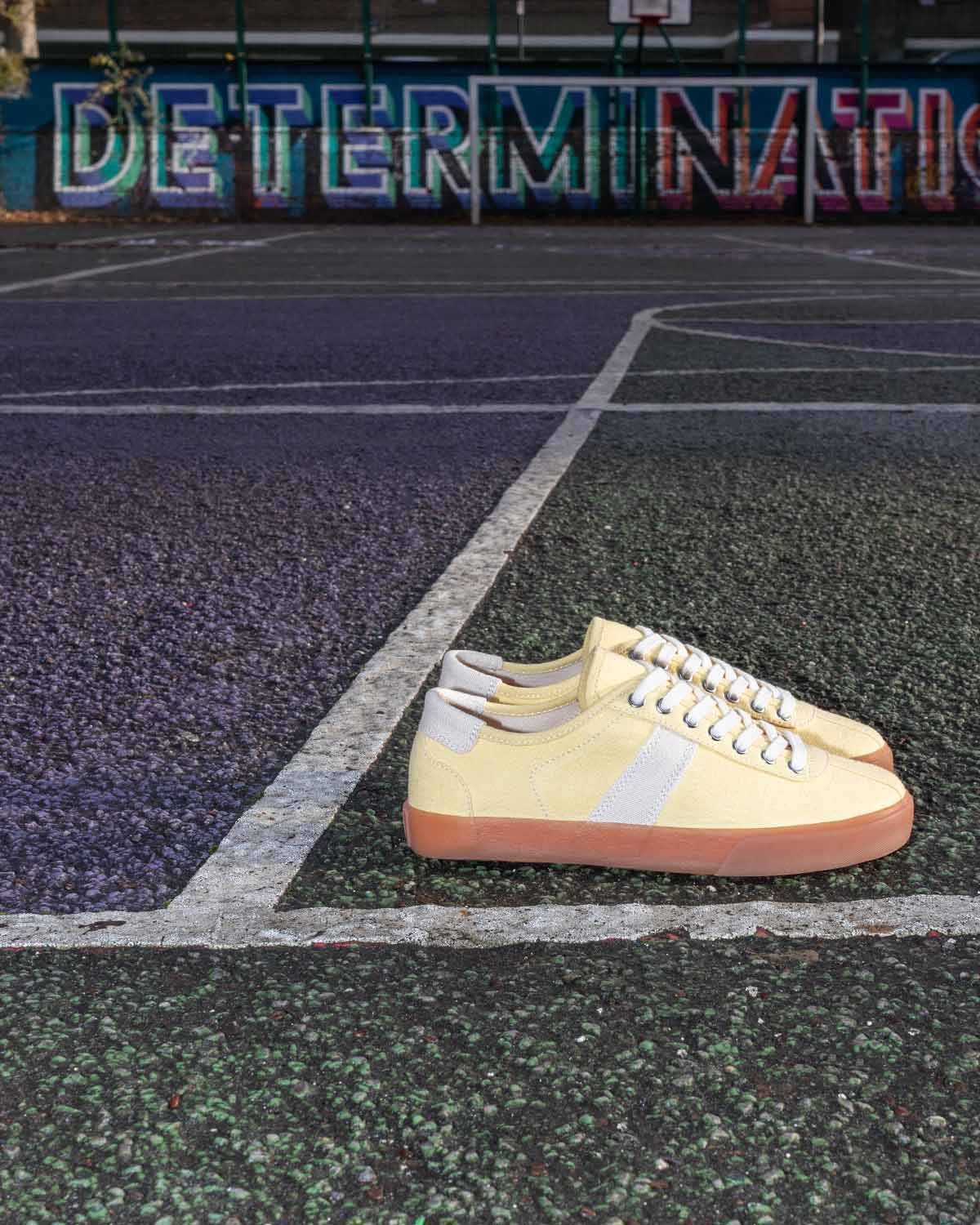 Looper Hemp Butter/Ecru trainers on an outdoor court in front of a mural reading Determination