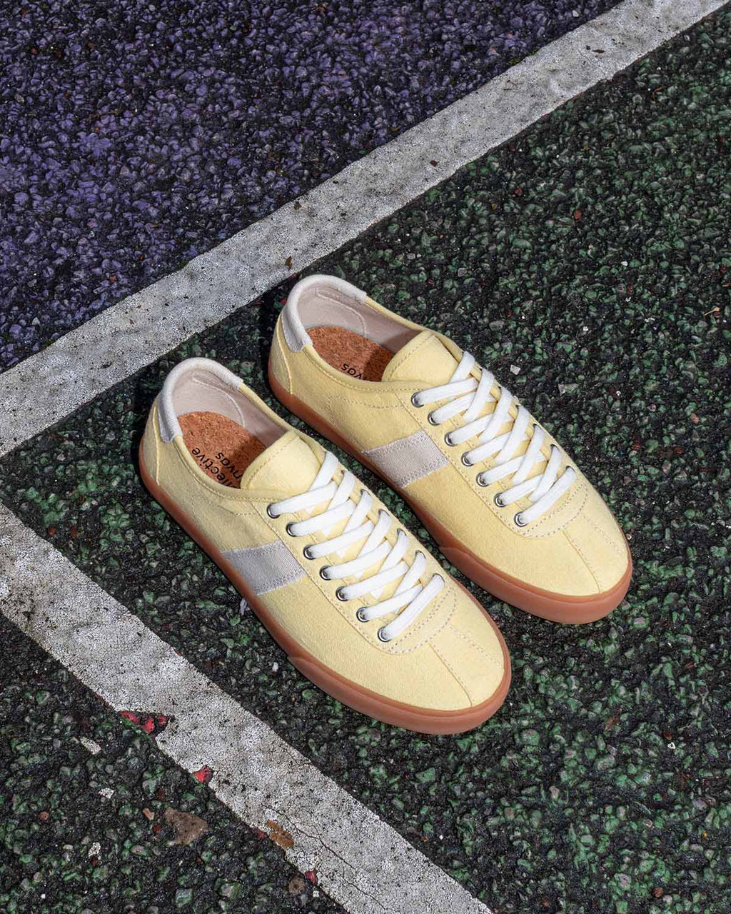Pair of Looper Hemp Butter/Ecru trainers on a speckled sports court beside a white line