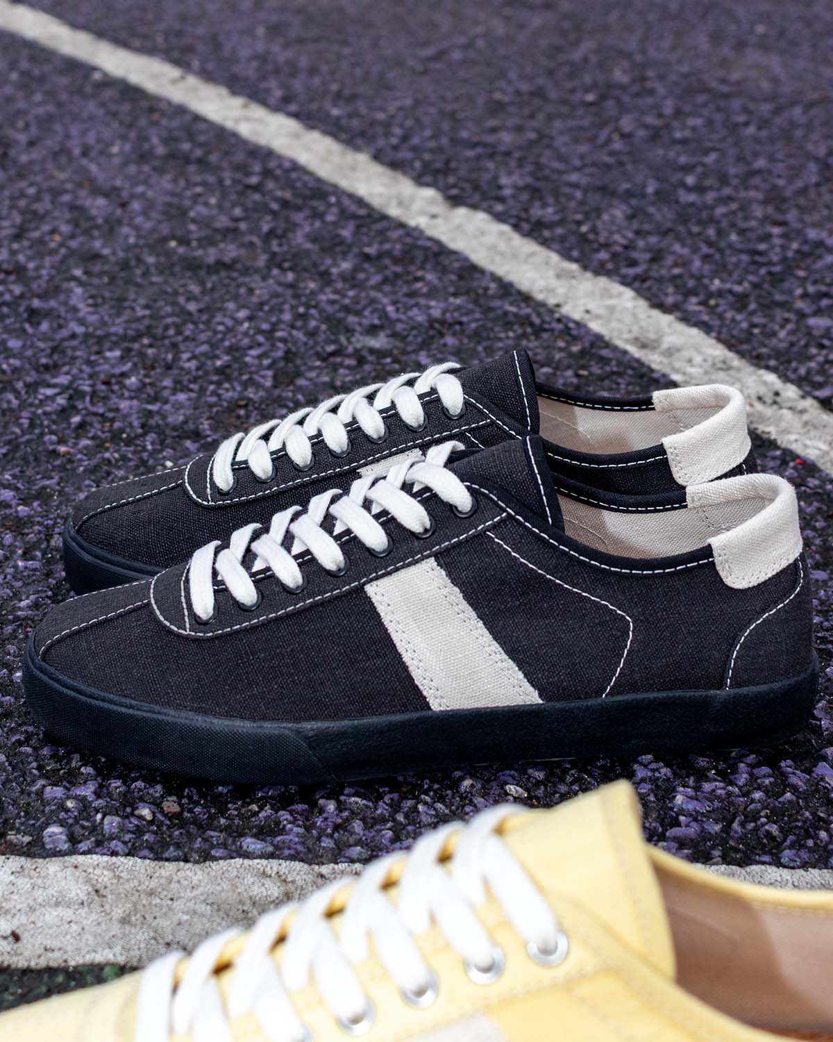 Looper Hemp Black/White Stitch trainers on a court surface beside a white line, a Butter/Ecru toe in view