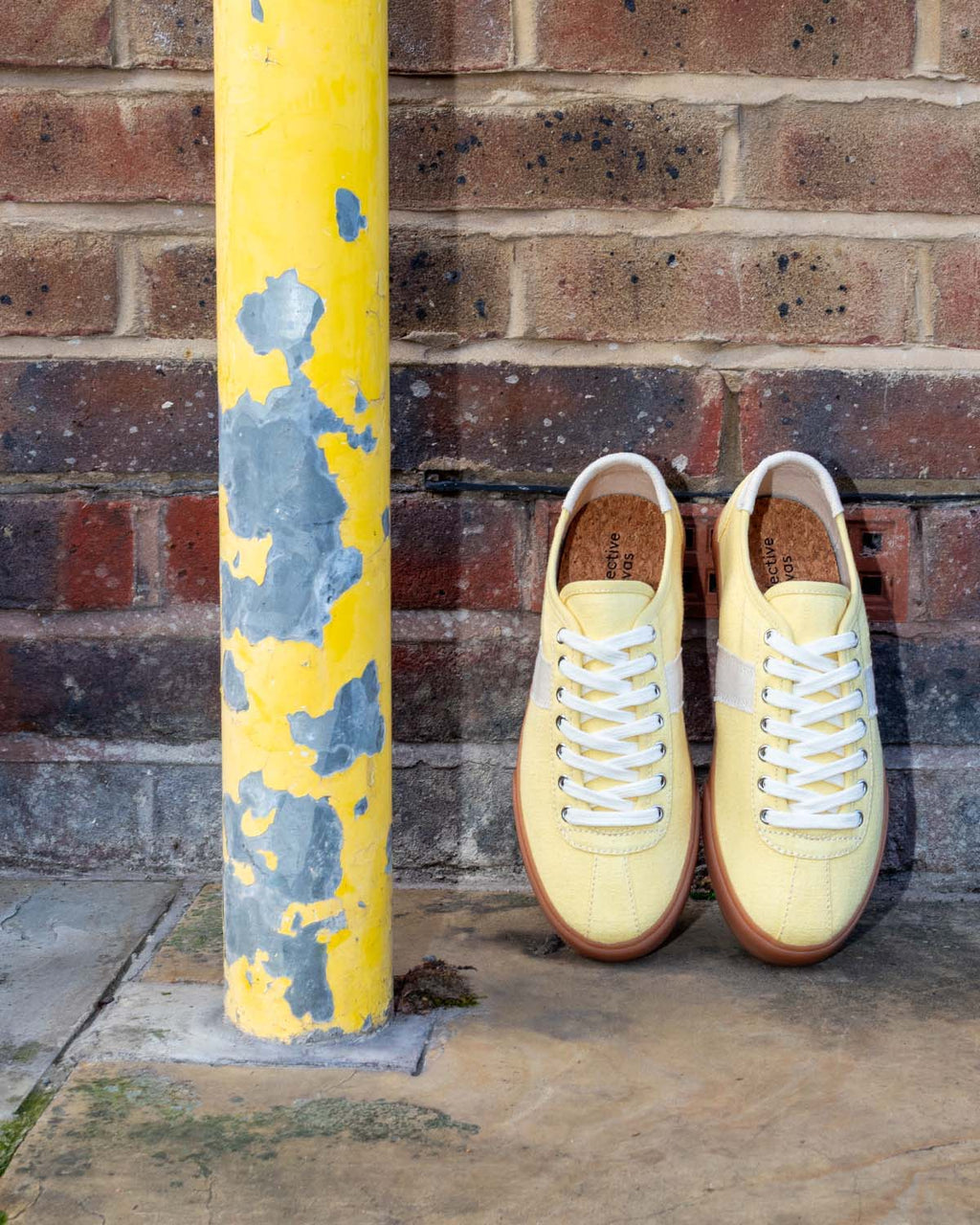 Looper Hemp Butter/Ecru trainers propped against a brick wall beside a peeling yellow post