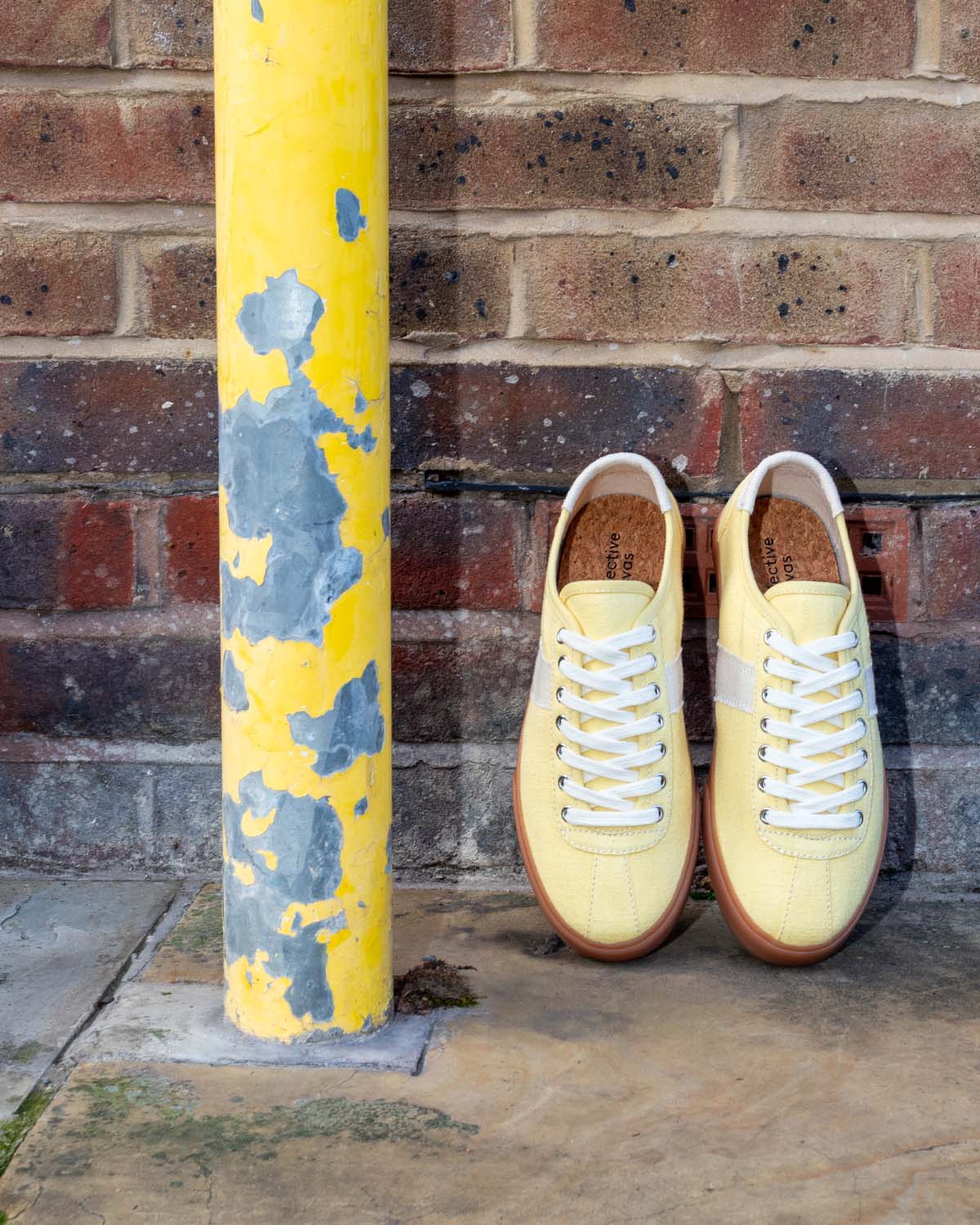 Looper Hemp Butter/Ecru trainers propped against a brick wall beside a peeling yellow post