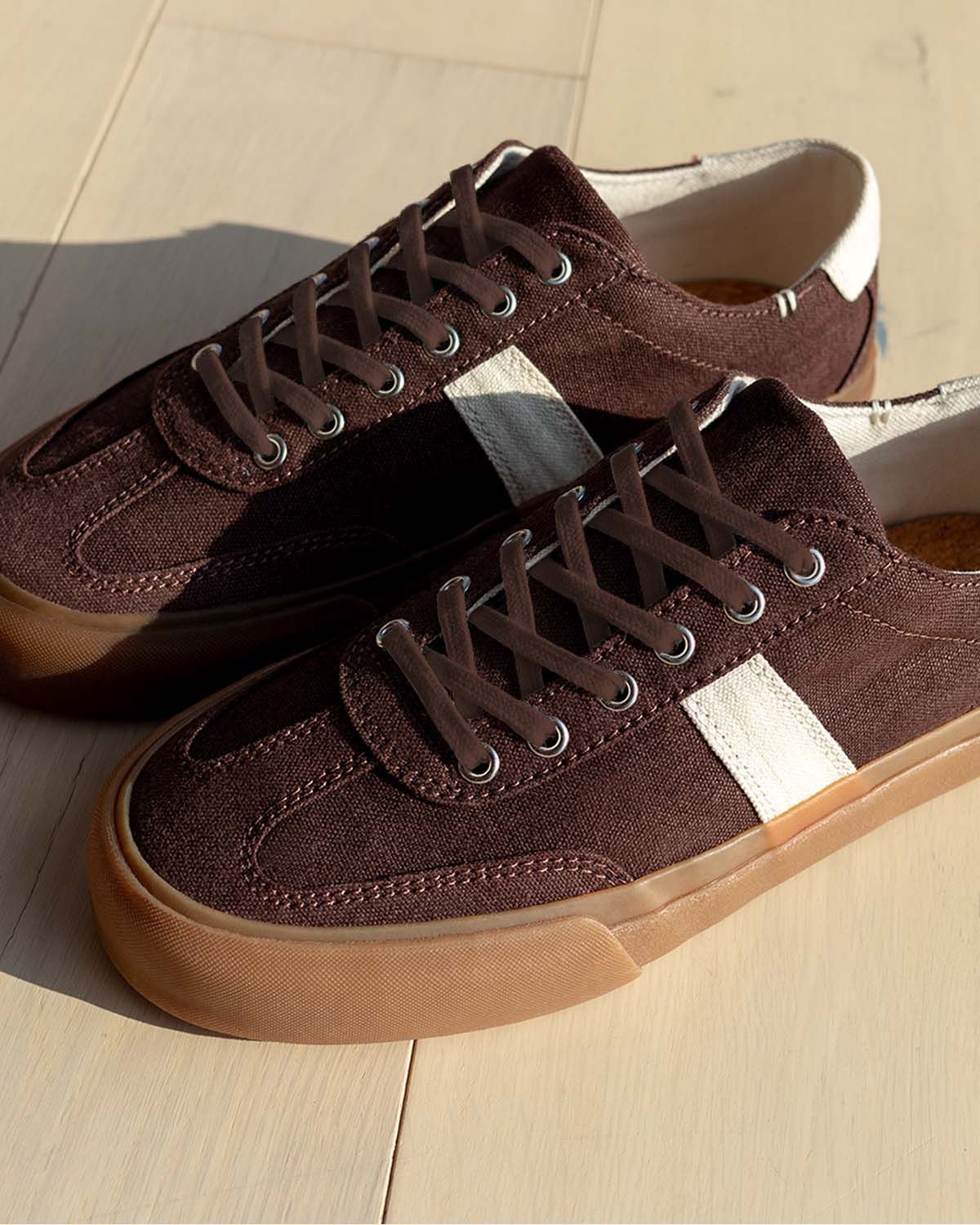 Veld Hemp Coffee/Ecru trainers on a pale wooden floor in sunlight, showing ecru stripes and cork insoles