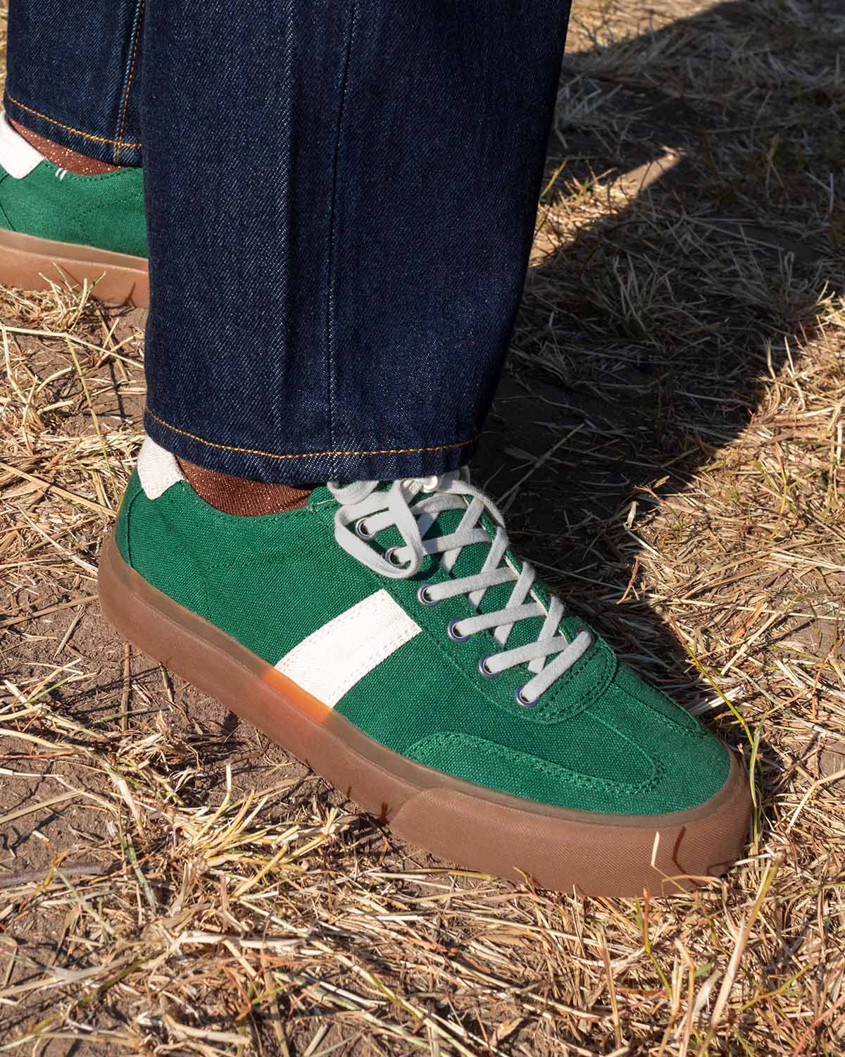 Wearing Veld Hemp Sage/Ecru trainers with dark denim, standing on dry grass