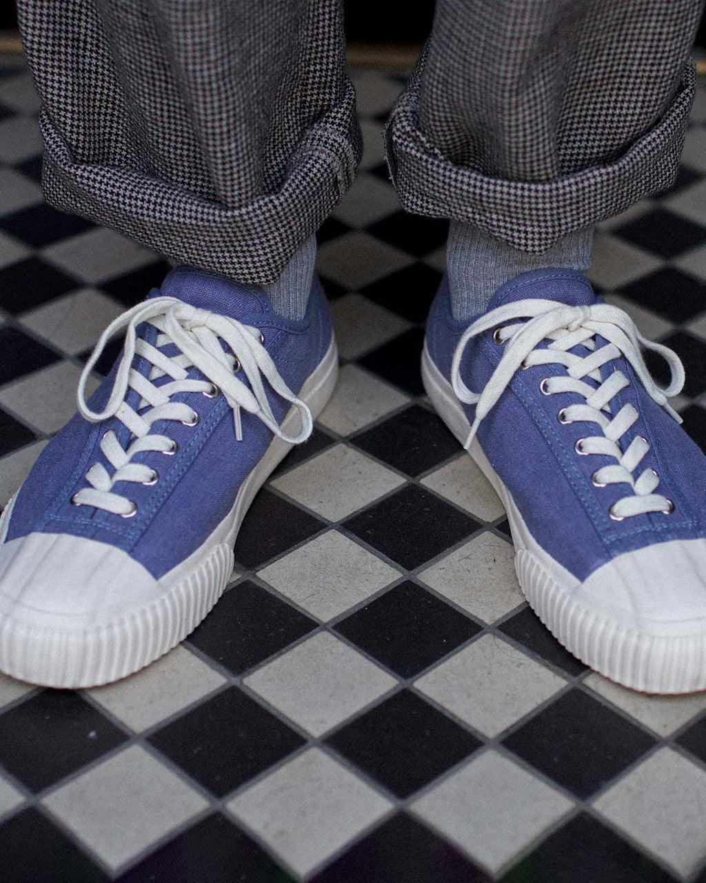 Wearing CC x Original Fibres Stonewash trainers with grey socks and cuffed check trousers on chequered tiles