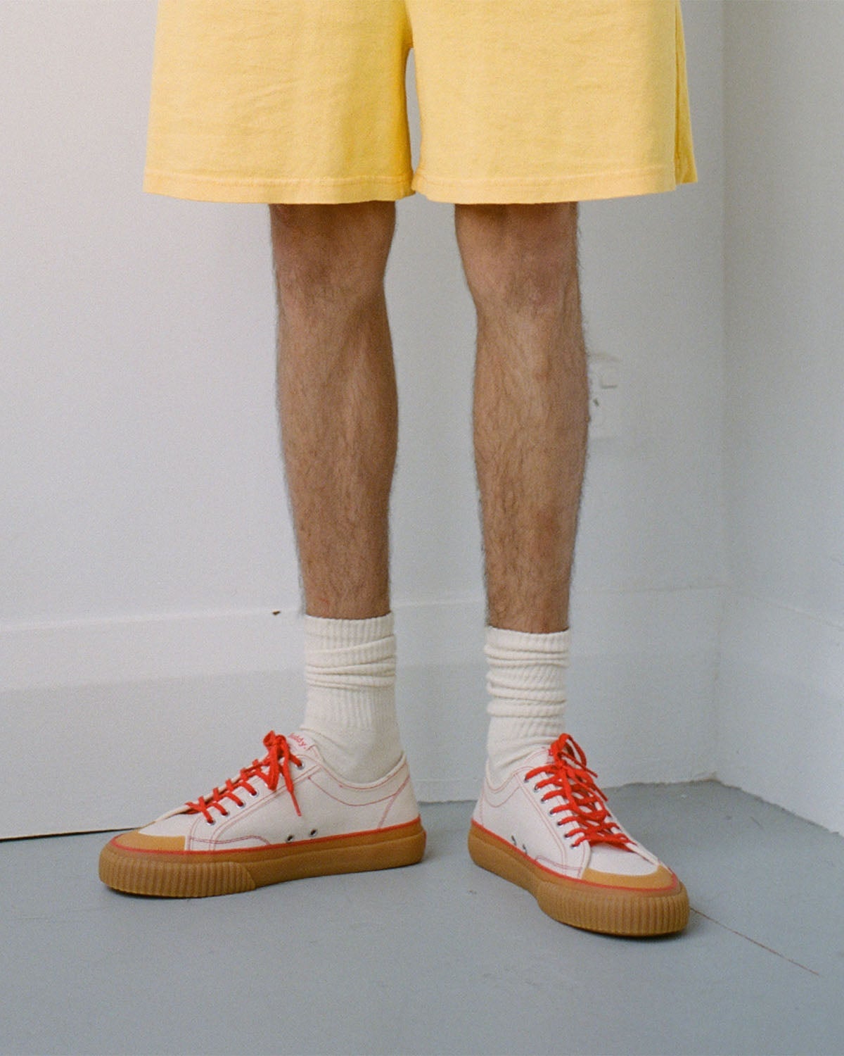 Wearing Buddy x CC Hemp Off-White/Red trainers with white socks and yellow shorts in a white room