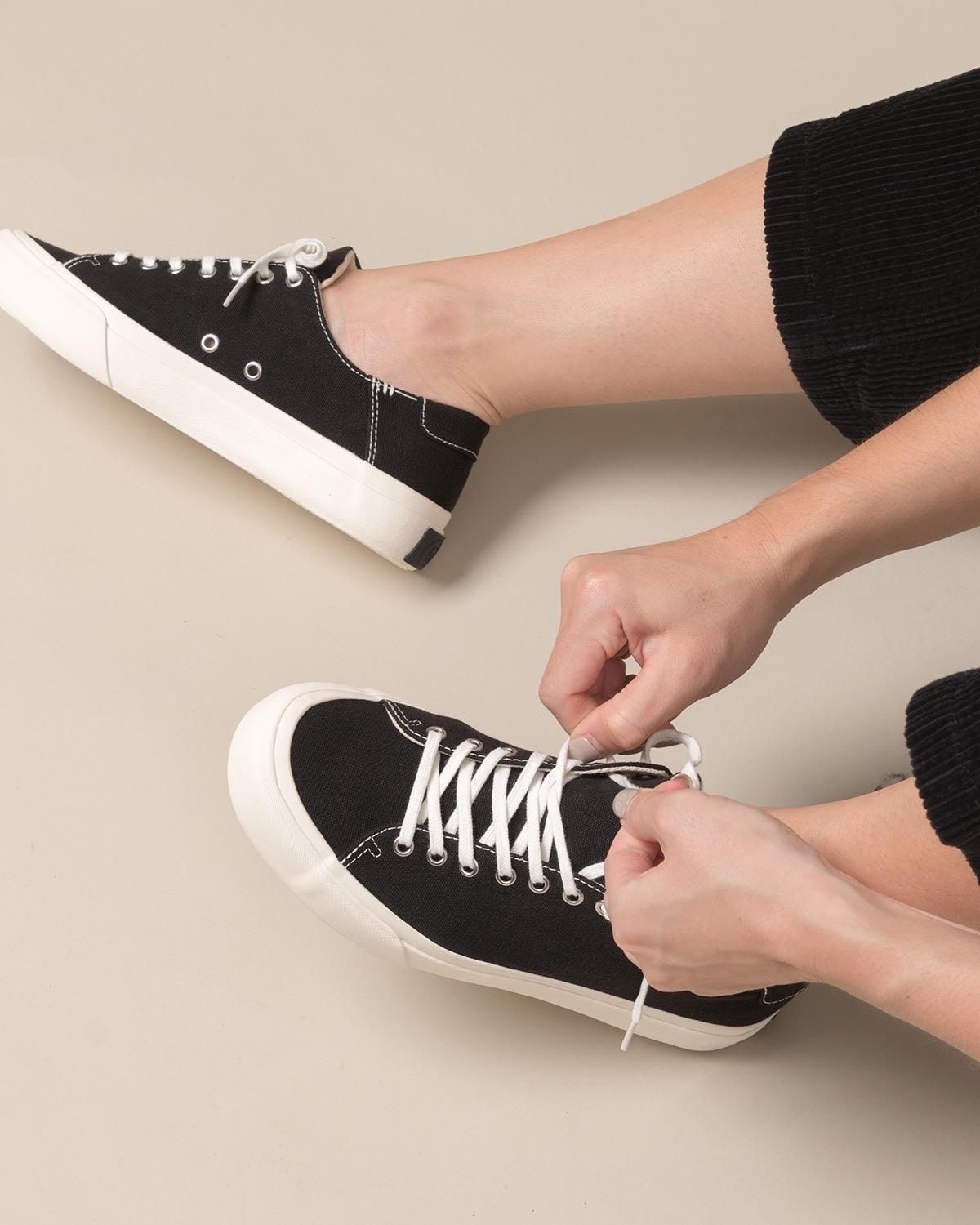 Tying the laces of Baan Black/White trainers, worn with cropped black trousers