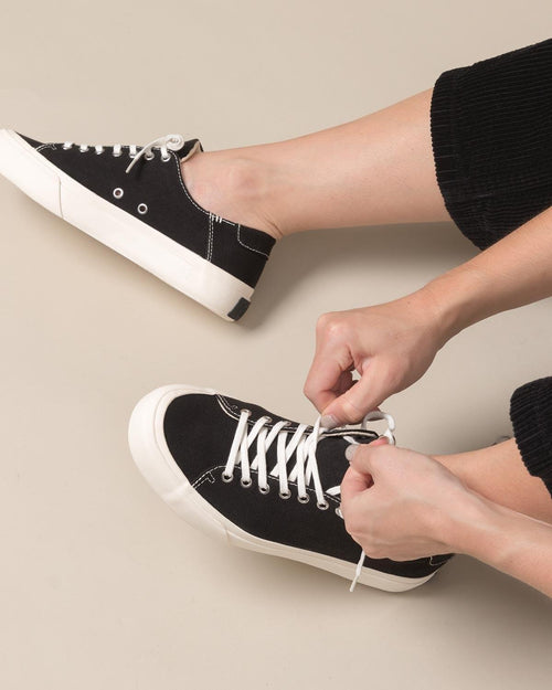 Tying the laces of Baan Black/White trainers, worn with cropped black trousers