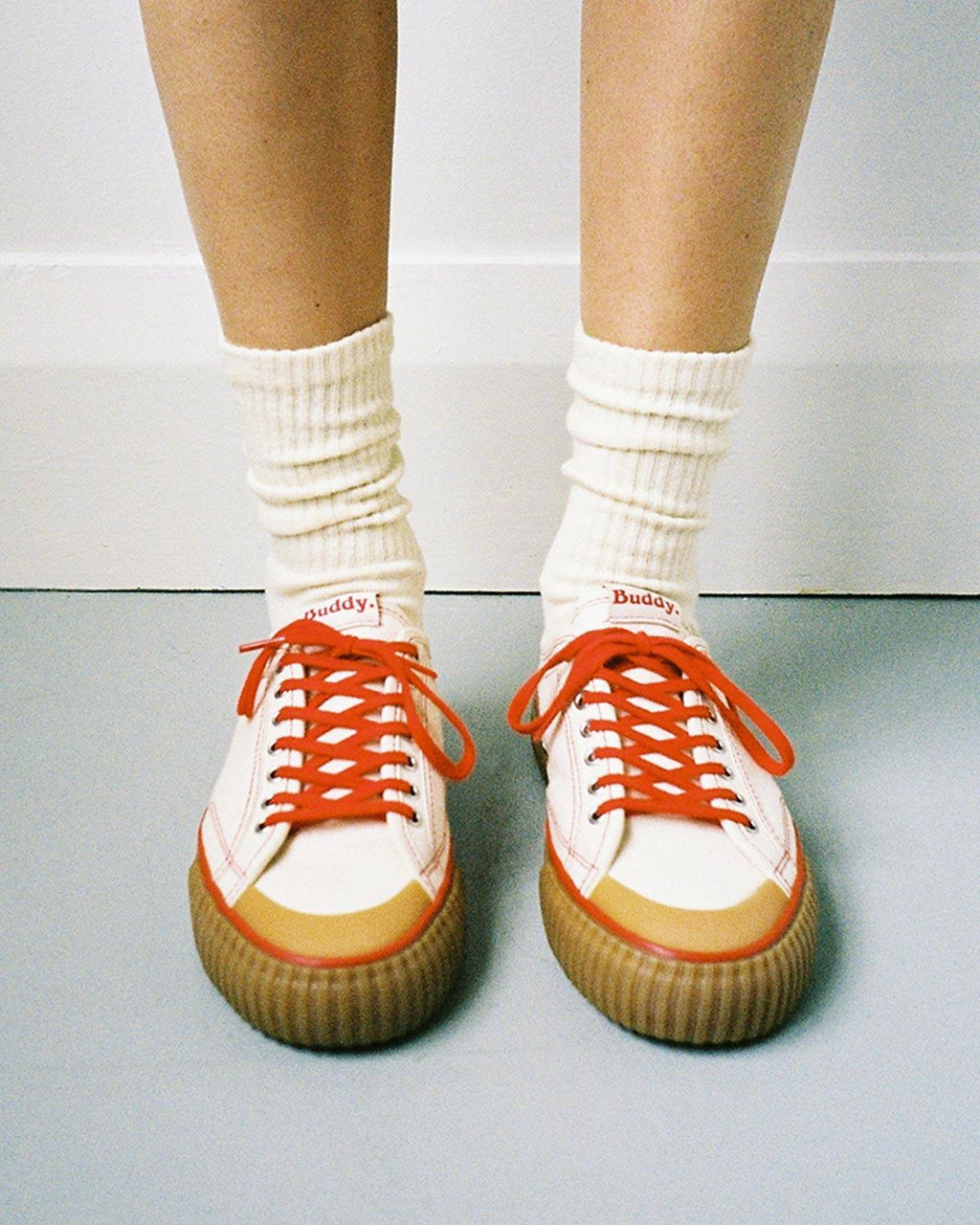 Wearing Buddy x CC Hemp Off-White/Red trainers with white slouch socks on a grey floor