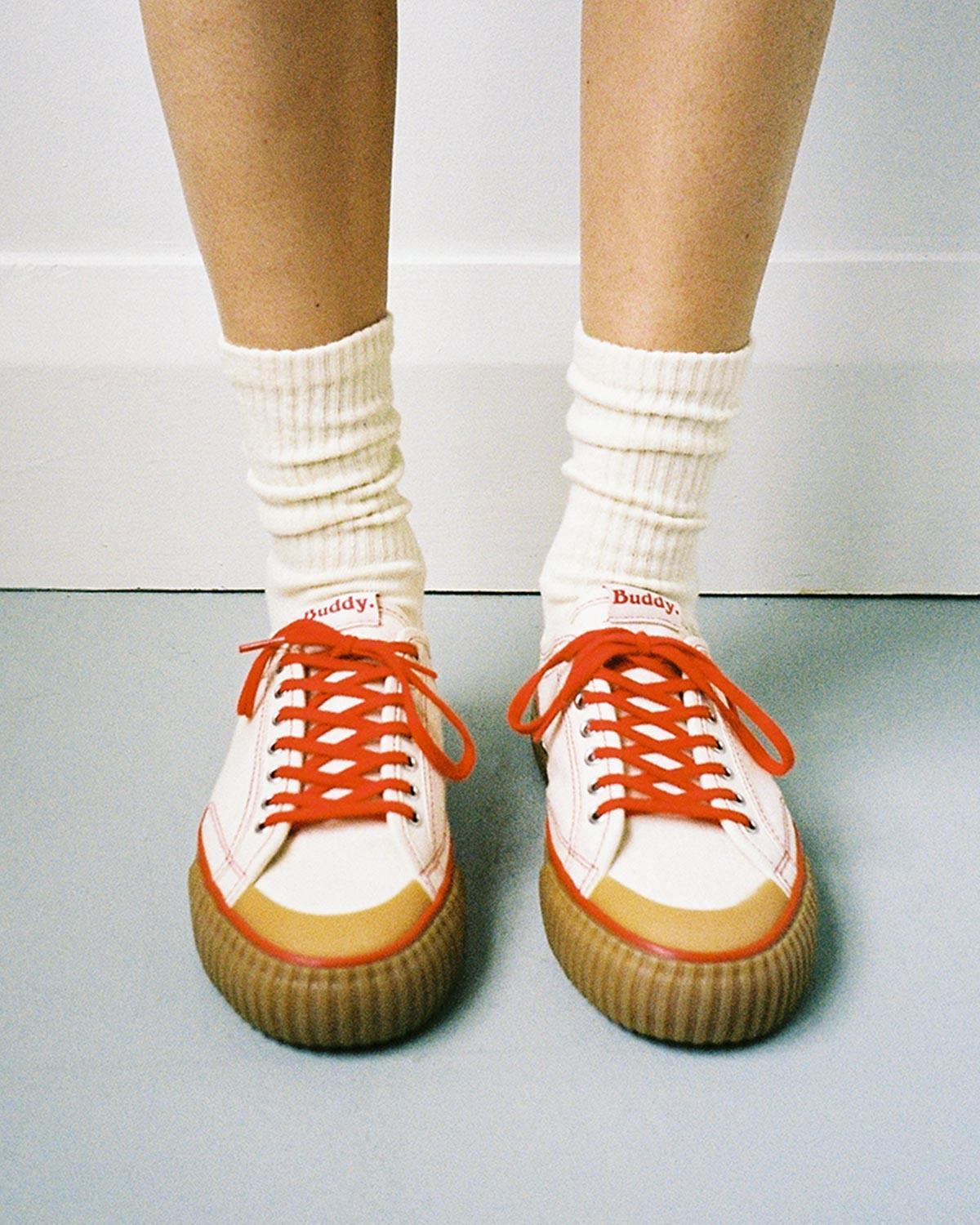 Wearing Buddy x CC Hemp Off-White/Red trainers with white slouch socks on a grey floor