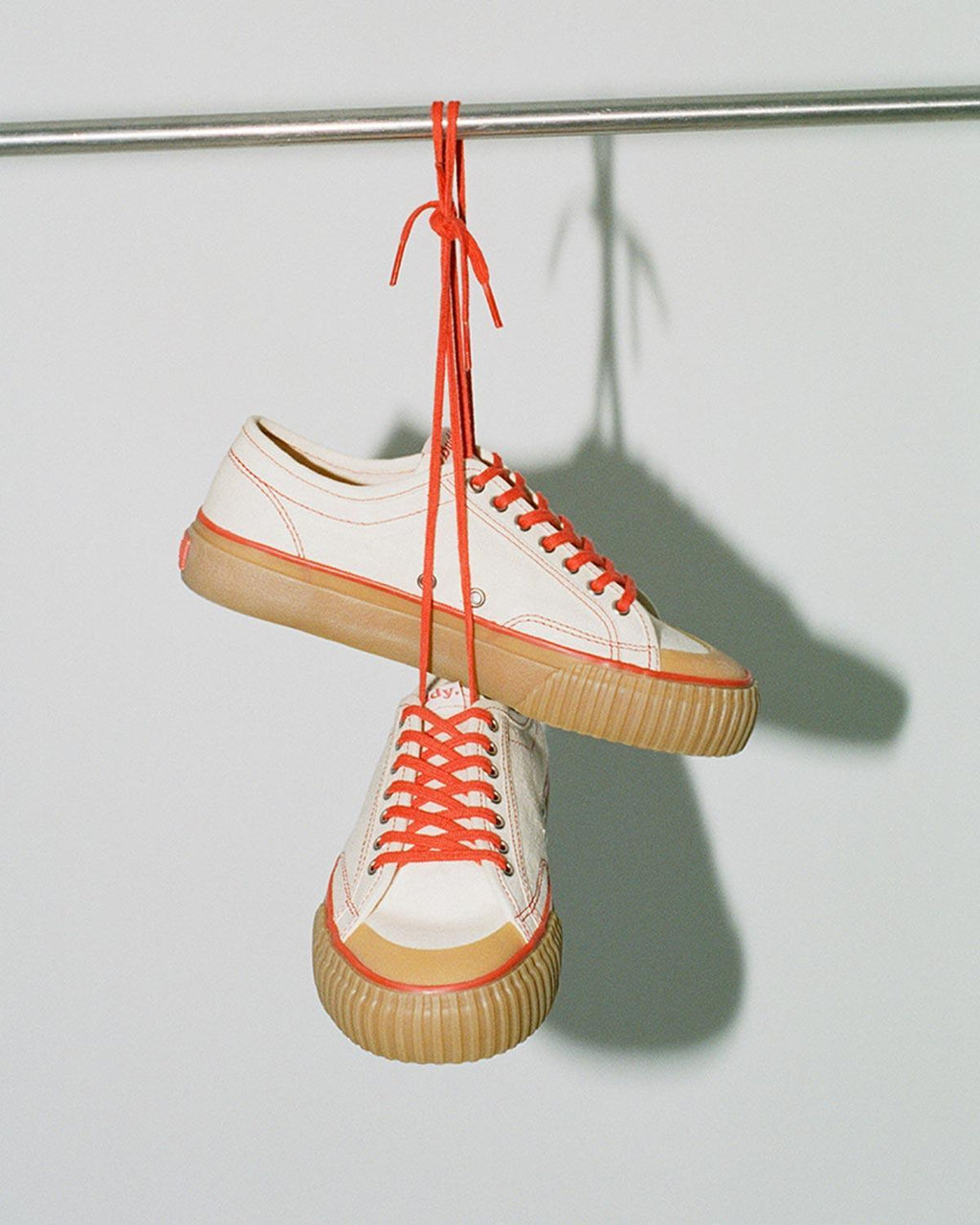Pair of Buddy x CC Hemp Off-White/Red trainers hanging by their red laces from a rail