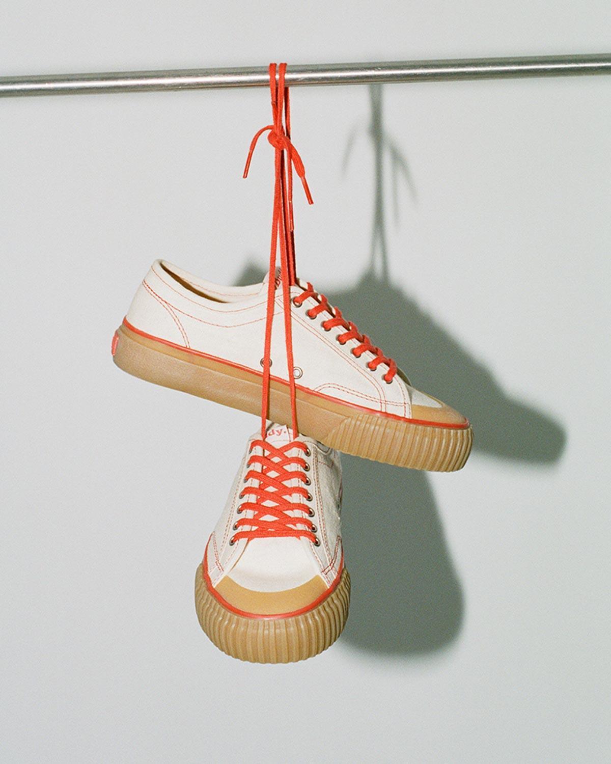 Pair of Buddy x CC Hemp Off-White/Red trainers hanging by their red laces from a rail